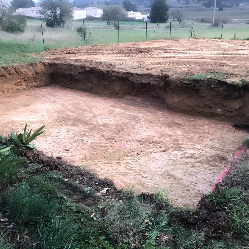 Excavation de fondation : Préparation du terrassement du chantier Vue d'une excavation de fondation rectangulaire profonde, avec des marquages roses au sol. Terrassement d'un futur chantier en pleine nature.