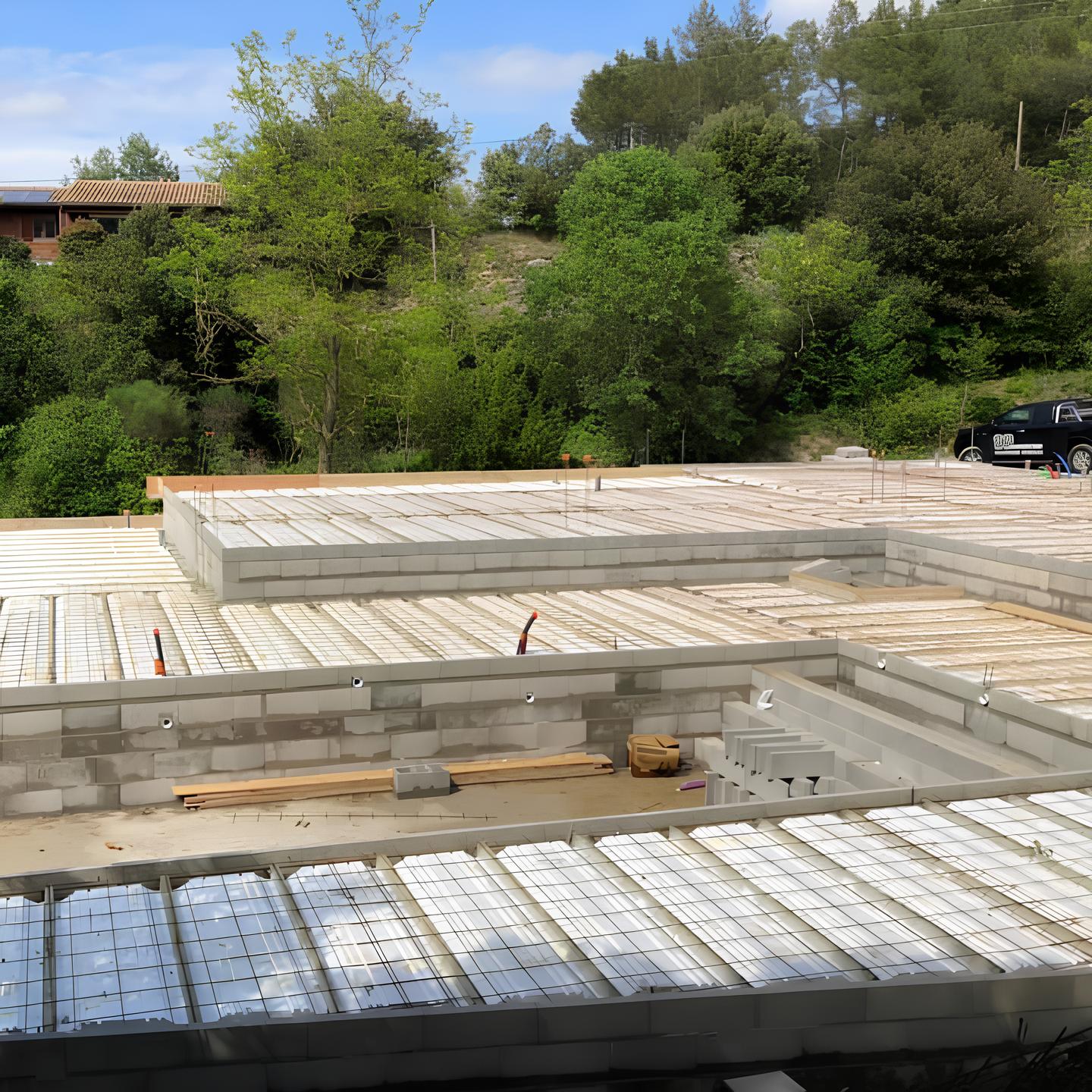 Gros œuvre d'une maison et piscine. Dalle et bassin en coffrage isolant avec ferraillage prêt à couler, devant un flanc de colline boisé.