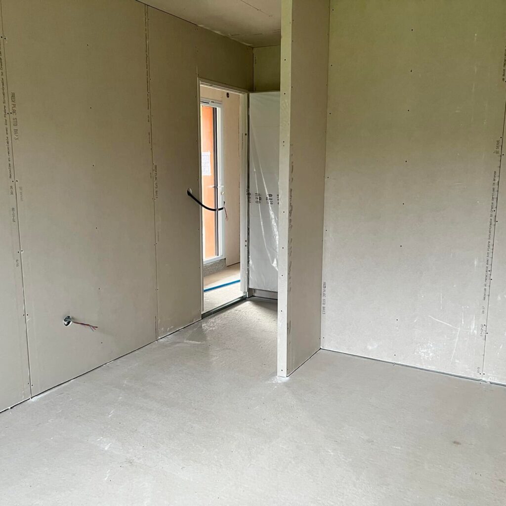 Pose de plaques de plâtre BA13 Frem Plac sur cloisons neuves. Cloisons intérieures en plaques de plâtre Frem Plac STD BA13, datées 27-11-22. Travaux de second œuvre, sol en ciment et passage de porte.